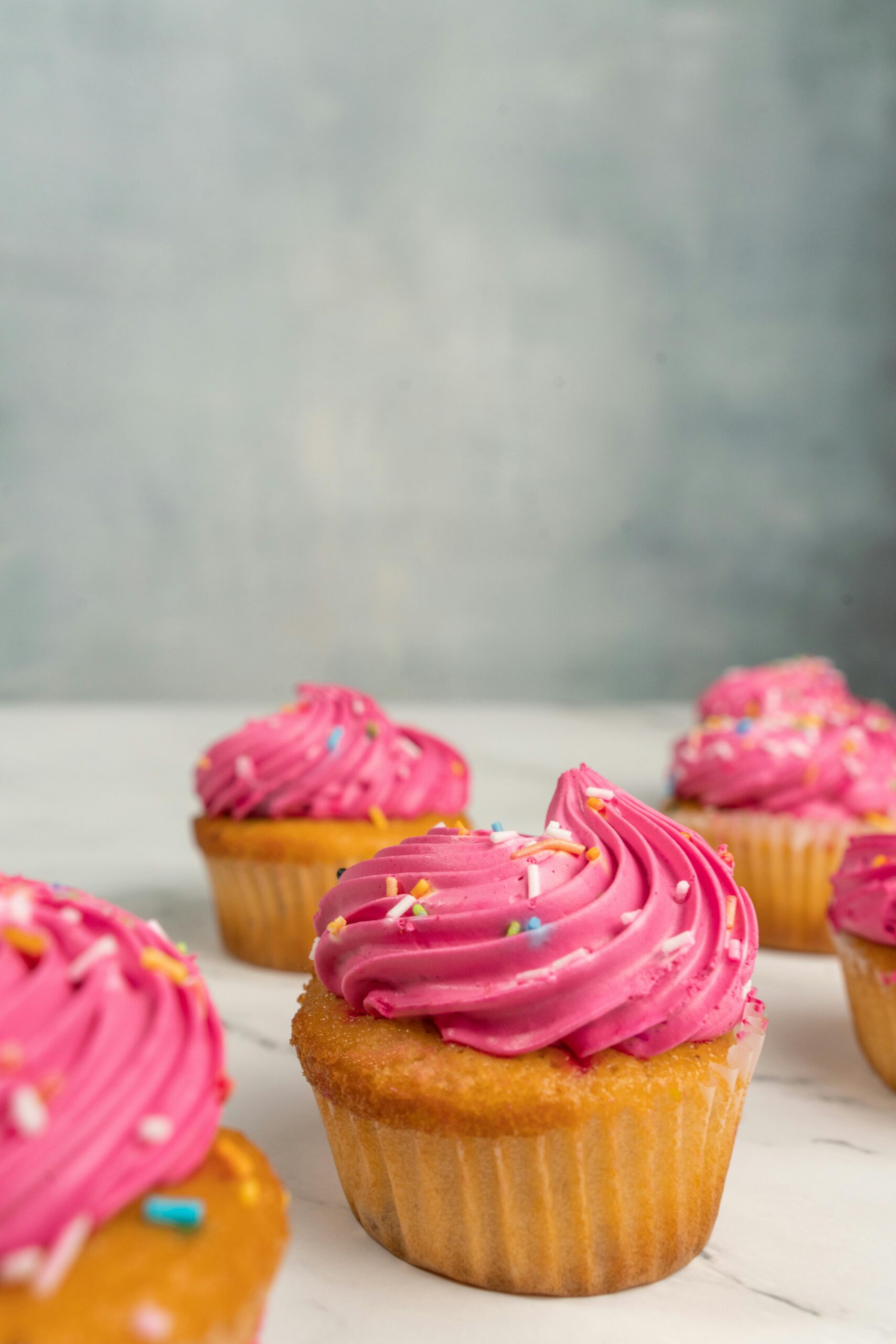 Vibrant cupcakes with pink frosting and sprinkles in a minimalist setting, perfect dessert display.